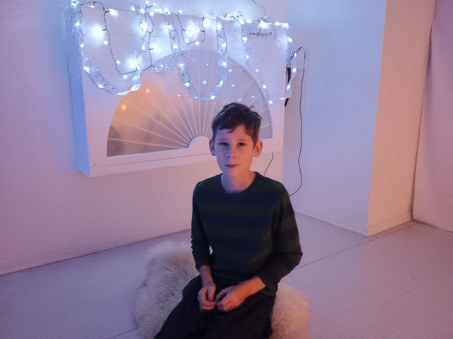 Viens zēns sēž uz grīdas baltajā istabā.