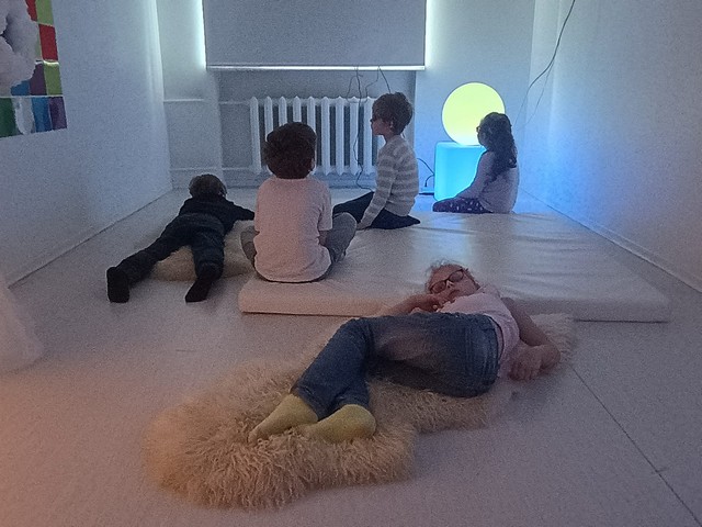 Pieci skolēni sēž un guļ uz matrača un segas un klausās.