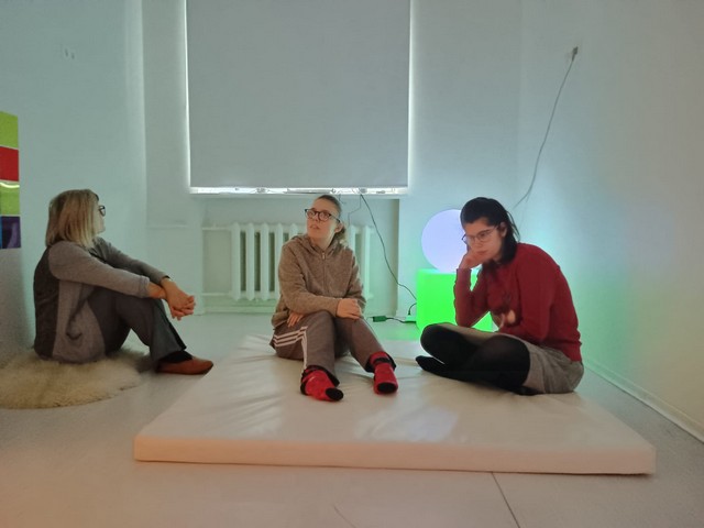 Trīs meitenes sēž Baltajā istabā un klausās.