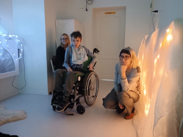 Divas skolotājas un zēns ratiņkrēslā baltajā istabā.