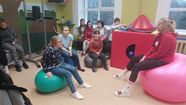 Skolotāja Argita sēž uz lielas piepūšamās bumbas un stāsta skolēniem un skolotājām.