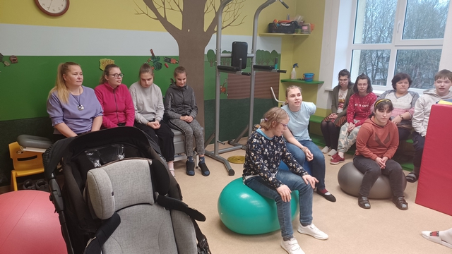 Bērni un skolotājas klausās sēžot bumbiņu istabā.