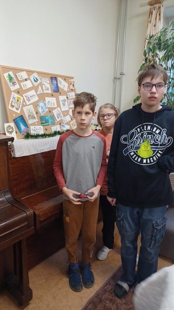 Trīs skolēni stāv pie stenda ar kartītēm