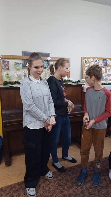 Divas meitenes un viens zēns stāv pie klavierēm, uz kurām ir stendi ar kartītēm.