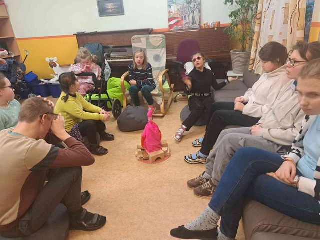 Skolēni Rotaļu istabā ap stilizētu ugunskuru.