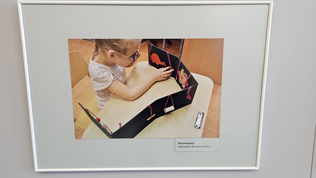 Meitene uz skolas sola skatās izliekamu grāmatu ar attēliem.