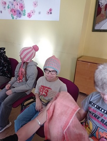 Trīs bērni sēž cepurēs un tur rokā segu.