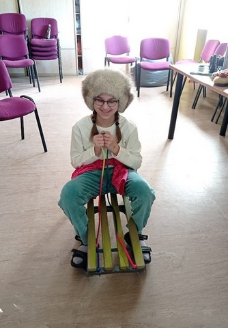 Meitene lielā cepurē sēž uz ragaviņām.