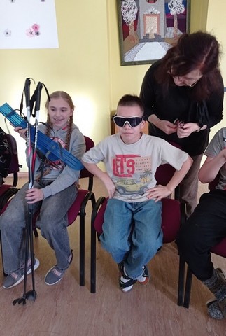 Zēns tumšās saules brillēs, meitene tur slēpju nūjas.