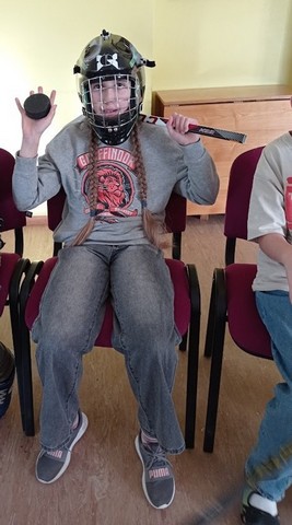 Zēns ar hokejista ķiveri un hokeja ripu un nūju rokās.