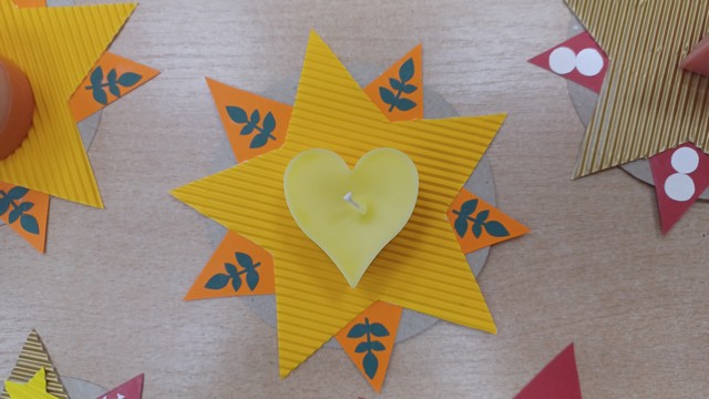Dzeltena papīra zvaigzne uz kuras dzeltena svece sirds formā.