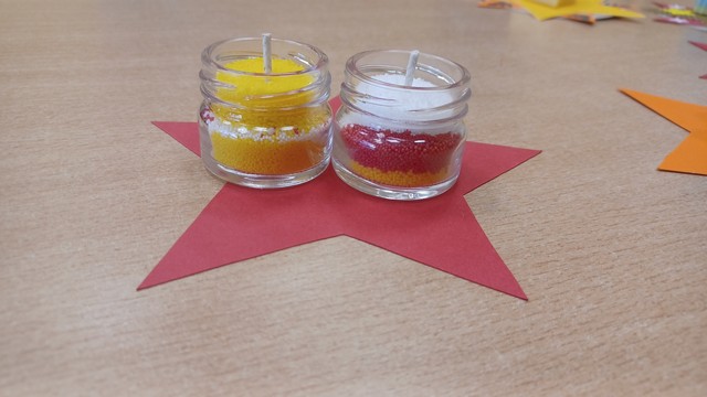 Uz galda viena papīra zvaigzne uz kuras divas burciņas ar svecēm.