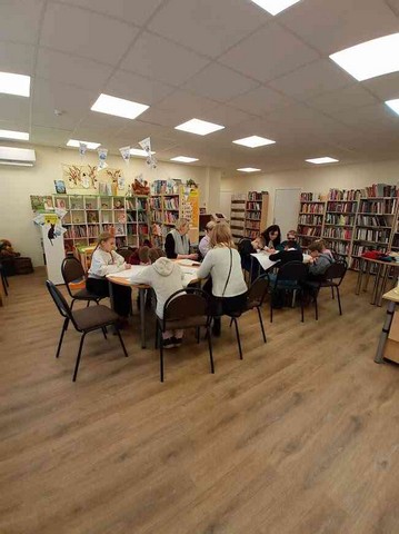 Visi sēž bibliotēkā pie galdiem.