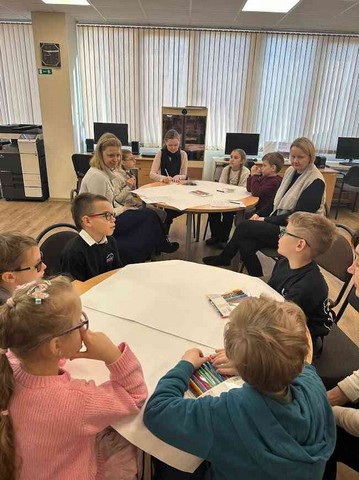 Skolēni sēž pie diviem apaļiem galdiem un gatavojas zīmēt.