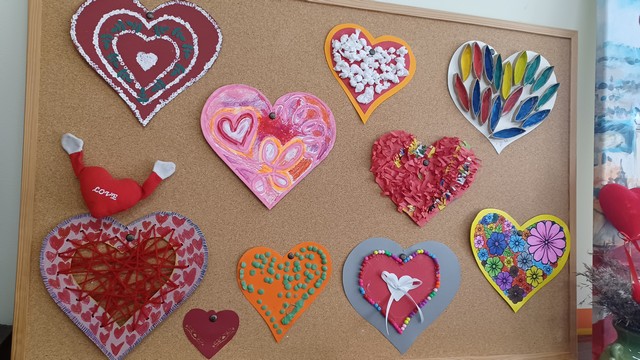 Pie tāfeles piespraustas 10 krāsainas papīra sirdis.