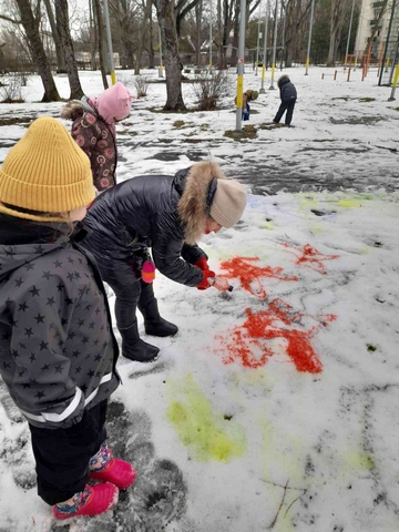 Trīs Skolēni ar sarkanu krāsu zīmē sniegā.