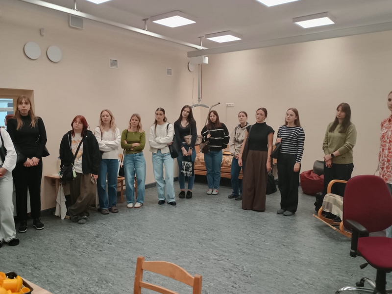 Studentes pusaplī stāv kādā klasē un klausās stāstījumu.