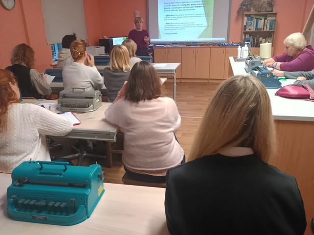 Klase ar interaktīvo tāfeli, apmeklētājas sēž krēslos.